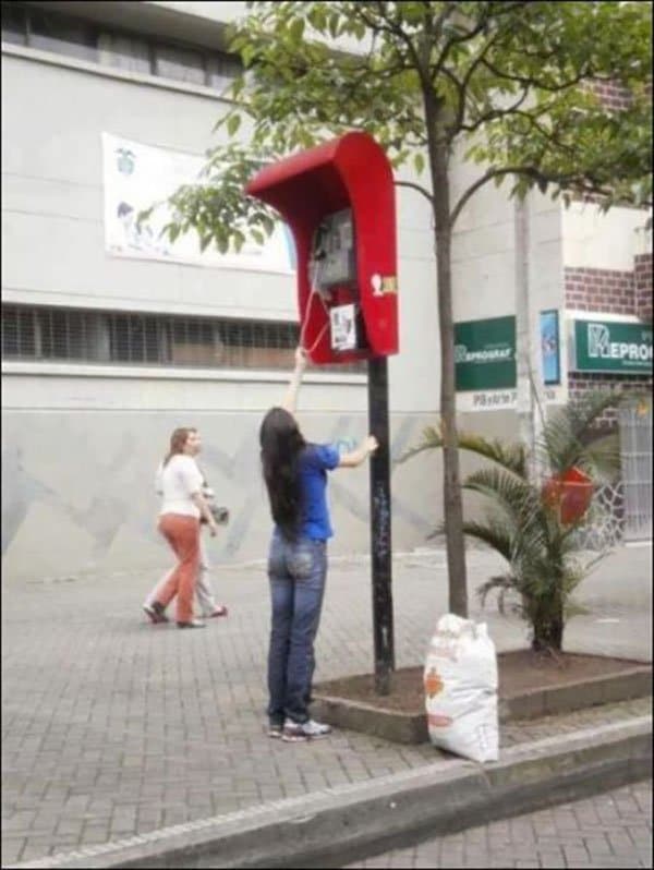 very tall red payphone with woman trying to reach