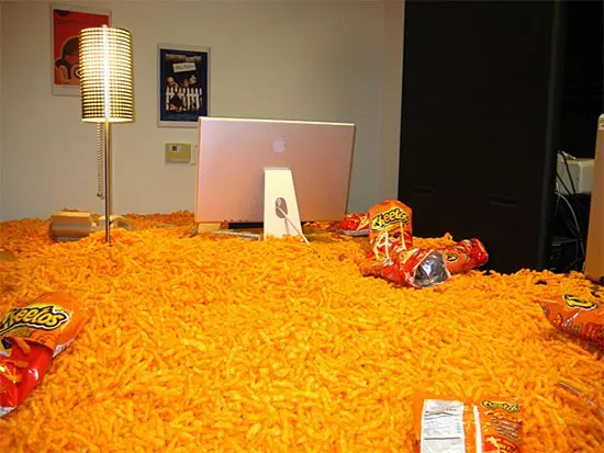 desk covered in thousands of cheetos with empty packets on top