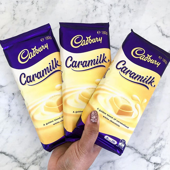 Hand Holding Three Packs of Cadbury's Caramilk