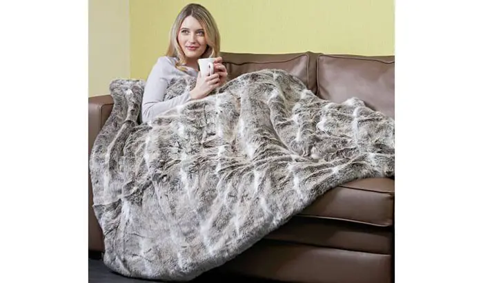 Lady on Couch Holding a Cup While Wrapped in Dreamland Alaskan Husky Faux Fur Heated Throw