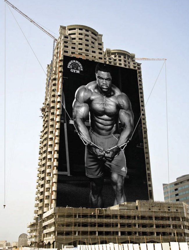 Powerhouse Gym Advertisement Featuring a Man Doing Cable Flyes on a Double-craned Construction Site