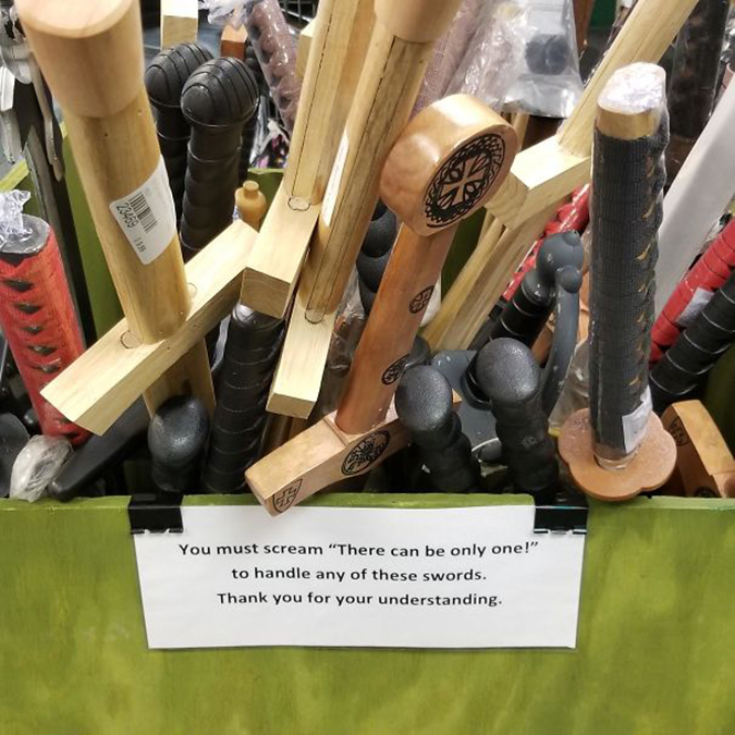 shop staff place a comical sign on their wooden sword display