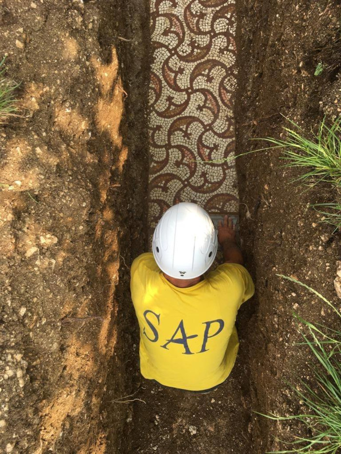 an archaeologist is pictured cleaning to soil off the surface of the ancient roman mosaic floor