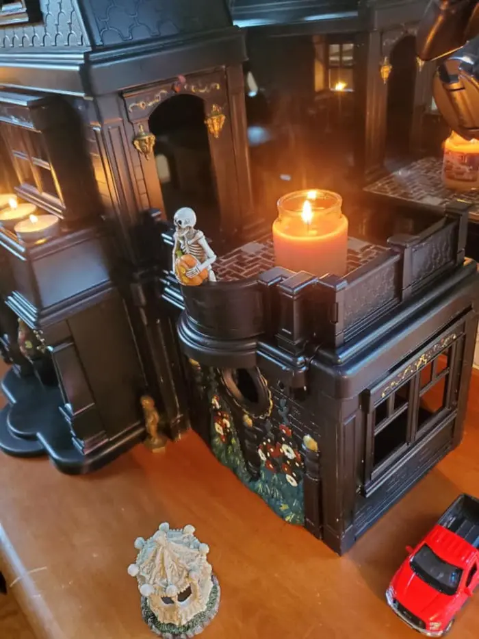 a skeleton holds a pumpkin while standing in the balcony of one of samantha's repainted dollhouses