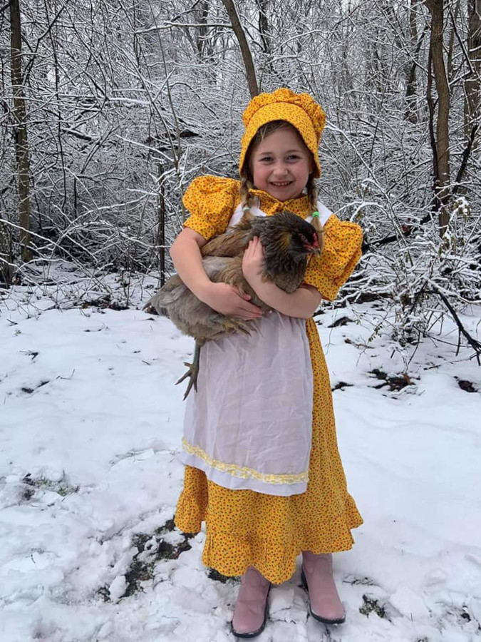 Melissa Tomas' daughter dons a yellow prairie dress and cuddlse a fluffy hen in the snow