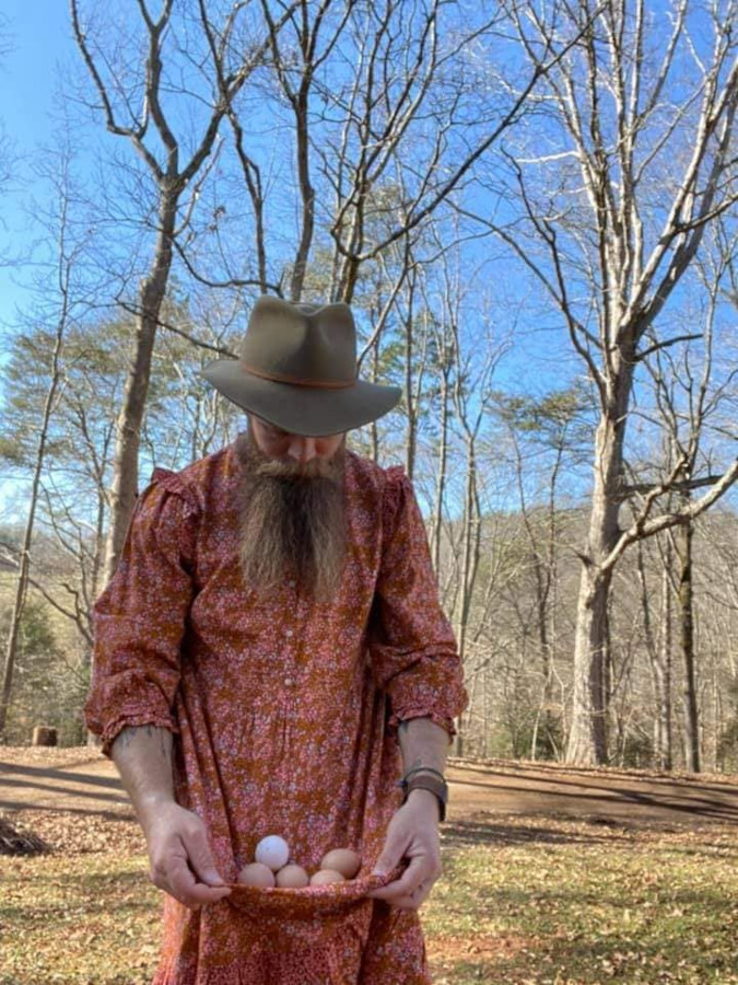 blond bearded man carries eggs using his dress' skirt